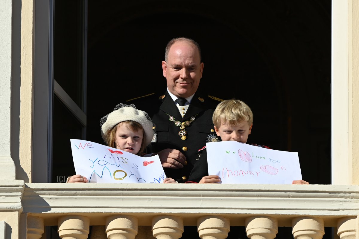 Prince Albert II of Monaco with his children Princess Gabriella of Monaco and Prince Jacques of Monaco showing "We miss you mom" and "Love you Mommy" drawings, appear at the Palace balcony during the Monaco National Day Celebrations on November 19, 2021 in Monte-Carlo, Monaco