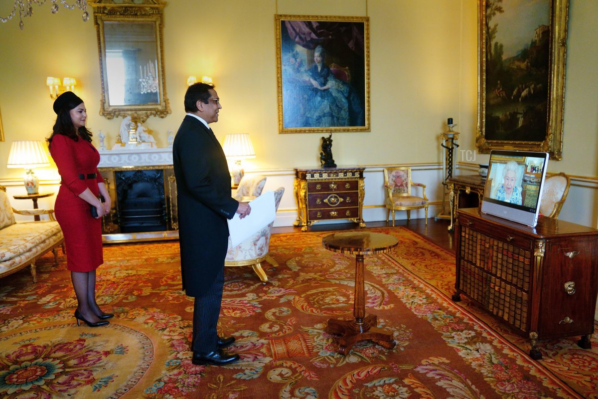 Queen Elizabeth II appears on a screen via videolink from Windsor Castle, where she is in residence, during a virtual audience to receive the High Commissioner of Trinidad and Tobago, Vishnu Dhanpaul (centre), and Mrs Geofroy-Dhanpaul (left), at Buckingham Palace on March 3, 2022 in London, England