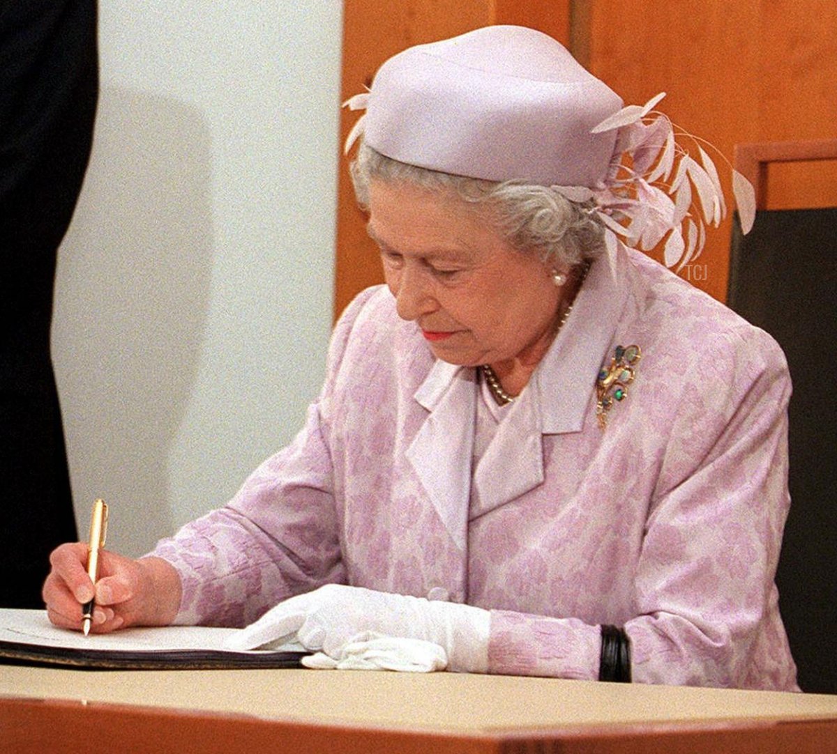 Britain's Queen Elizabeth II signs the visitor's book at Parliament House in Canberra 27 March 2000 as Australian Prime Minister John Howard stands in the background