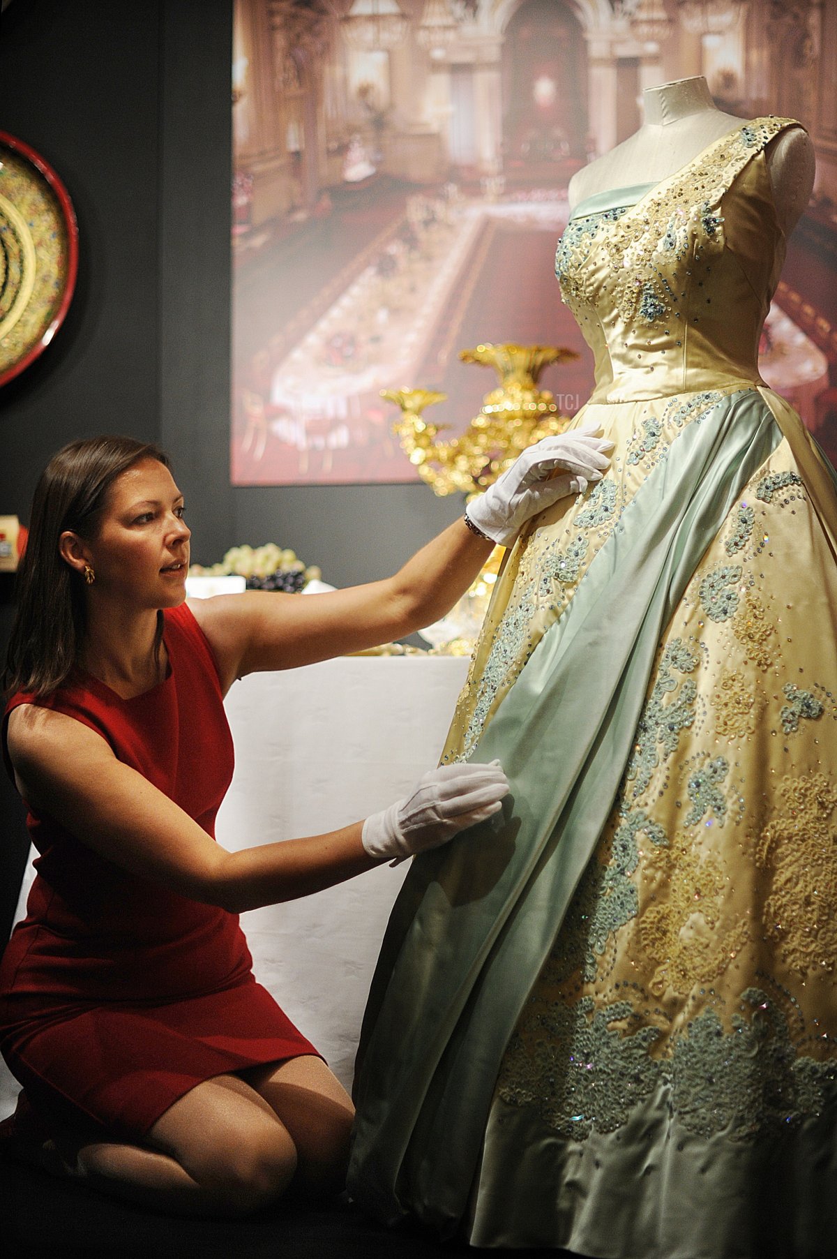 A curator poses for photographs with an evening dress worn by Britain's Queen Elizabeth II during a state visit to the Netherlands in 1958 which forms a part of "The Queen's Year" exhibition at Buckingham Palace in central London, on July 23, 2010