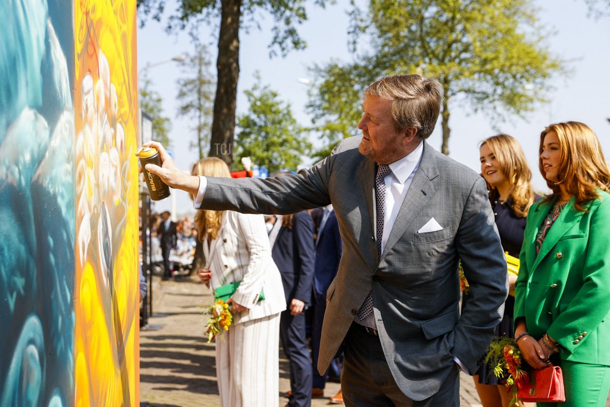 King Willem-Alexander of the Netherlands (L) sprays paint on a mural flanked by Princess Ariane (2nd R) and Princess Alexia (R) during a gathering for King's Day in Maastricht, on April 27, 2022