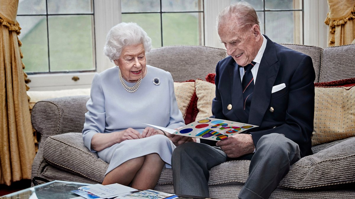 In this handout image released on November 19, Queen Elizabeth II and Prince Philip, Duke of Edinburgh look at their homemade wedding anniversary card, given to them by their great grandchildren Prince George, Princess Charlotte and Prince Louis, in the Oak Room at Windsor Castle ahead of their 73rd wedding anniversary, on November 17, 2020 in Windsor, England