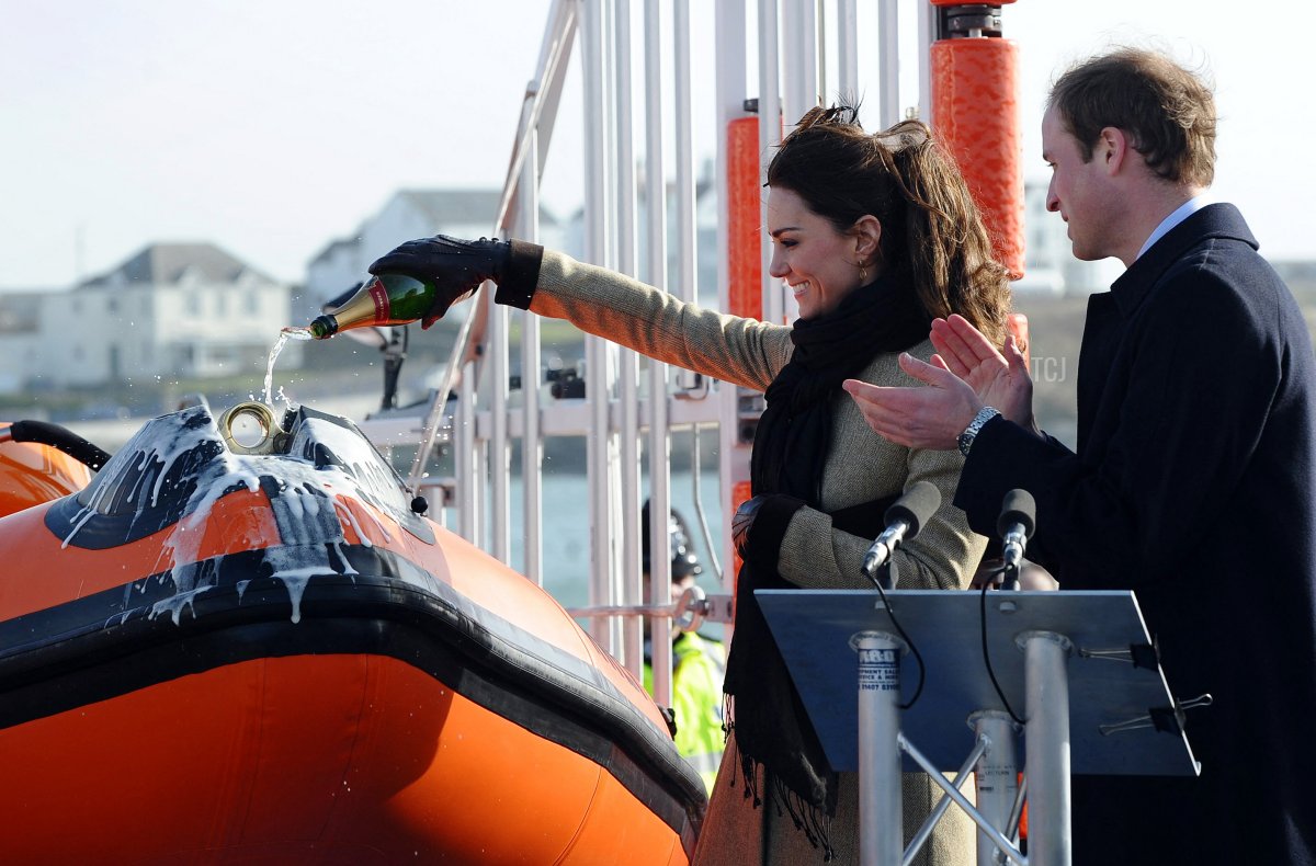 Britain's Prince William applauds while fiancee Kate Middleton (L) pours champagne over a lifeboat at the RNLI Lifeboat Station in Anglesey, near Bangor in Wales on February 24, 2011