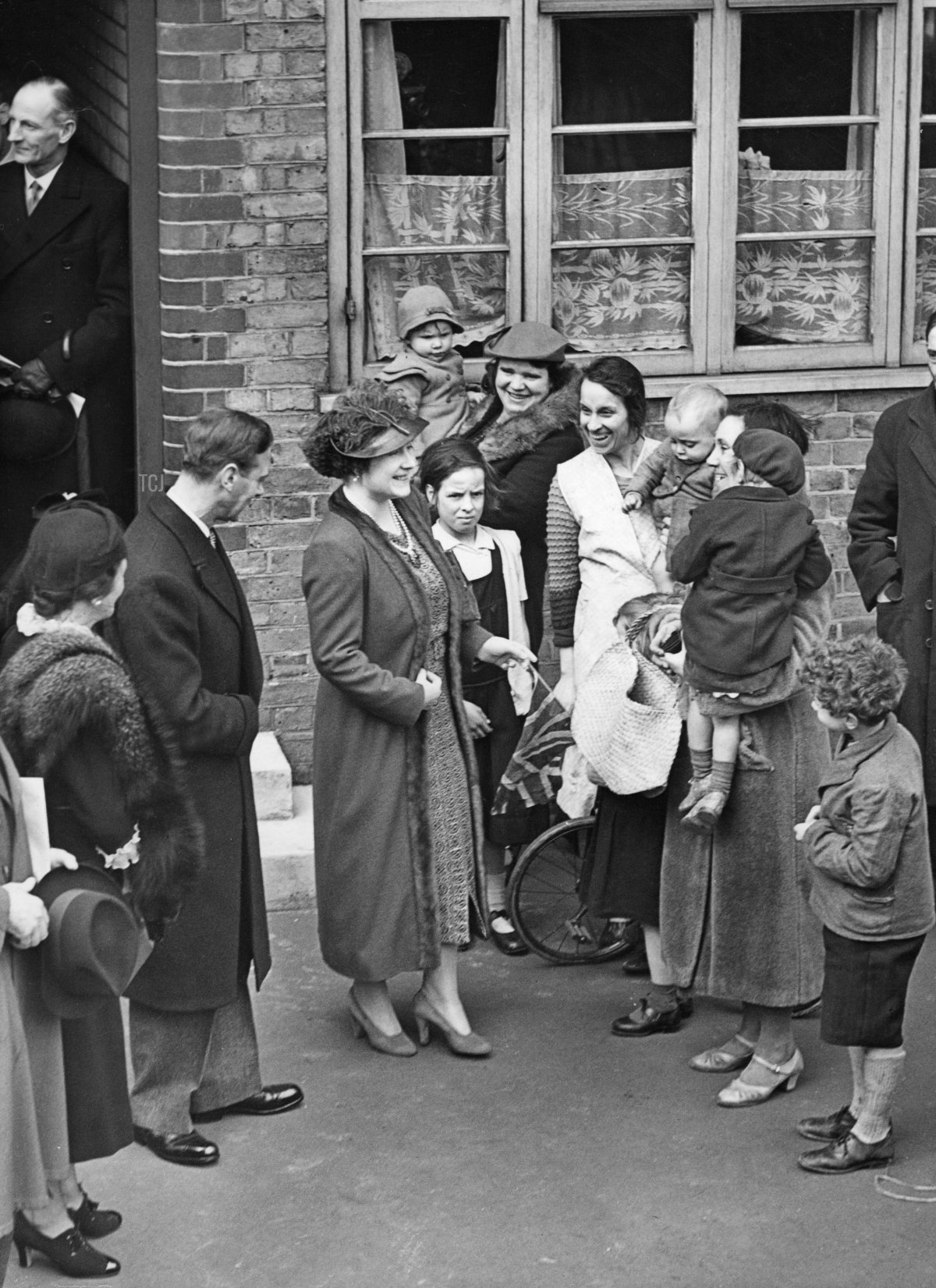 King George VI and Queen Elizabeth in London, 1938. King George VI (2nd from left) and Queen Elizabeth (3rd from left) visit the poorer districts in South London. Here in conversation with the residents of the McManus House in Battersea. Date created: 16/03/1938