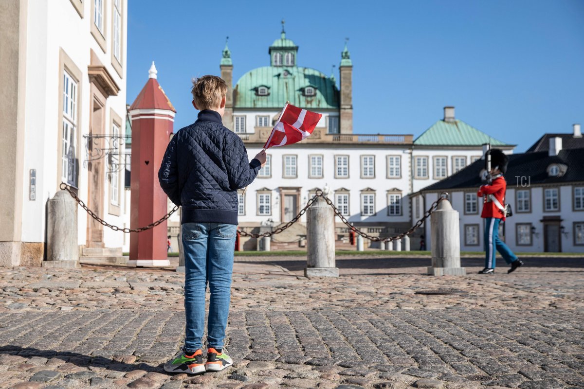 A boy waves a Danish flag in front of Fredensborg Palace in Fredensborg, Denmark, on April 16, 2020, the 80th birthday of Queen Margrethe II of Denmark, which she is celebrating in private due to the new coronavirus pandemic (OLAFUR STEINAR GESTSSON/Ritzau Scanpix/AFP via Getty Images)