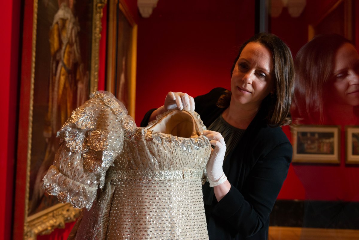 A curator adjusts the wedding dress of Princess Charlotte of Wales (1796-1817), on display in 2023 at the Queen's Gallery, Buckingham Palace (Royal Collection Trust)