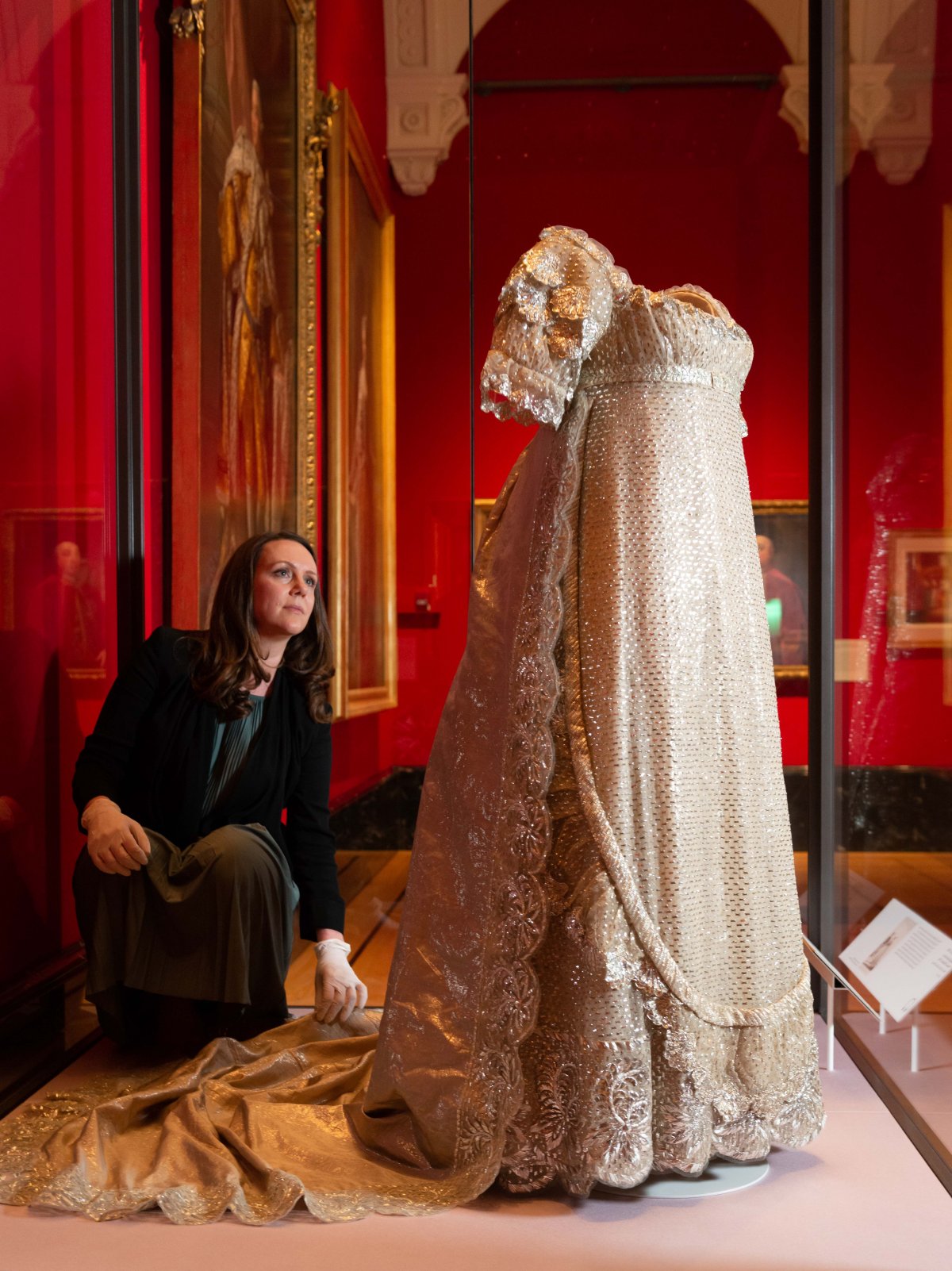 A curator adjusts the wedding dress of Princess Charlotte of Wales (1796-1817), on display in 2023 at the Queen's Gallery, Buckingham Palace (Royal Collection Trust)