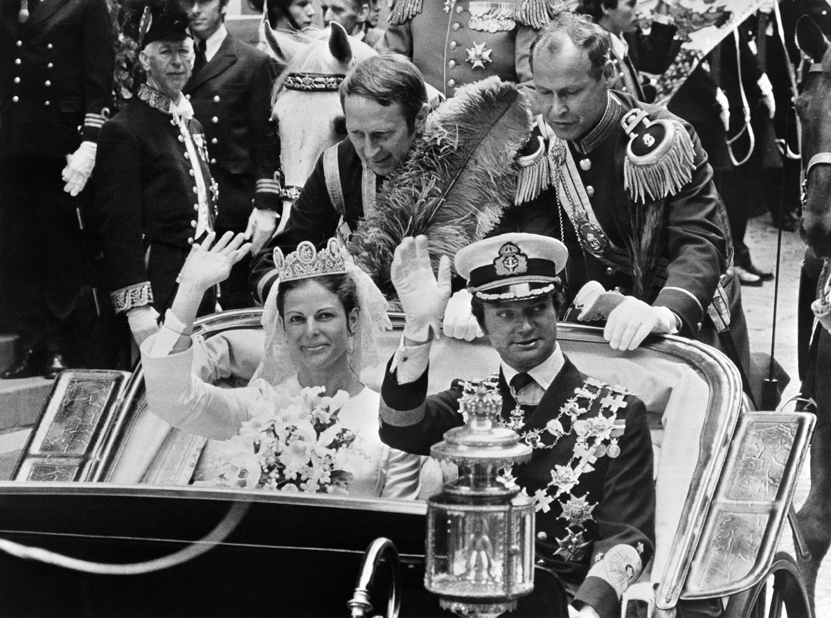 King Carl XVI Gustaf and Queen Silvia of Sweden wave during a carriage procession after their royal wedding in Stockholm on June 19, 1976 (AFP via Getty Images)