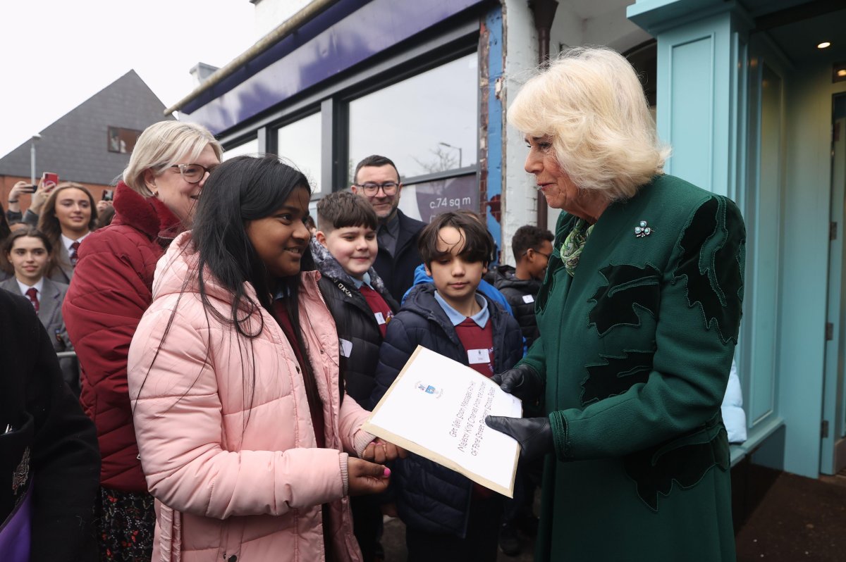Queen Camilla of the United Kingdom receives a packet of "Get Well Soon" messages for King Charles from the children of Fane Street Primary School during a visit to Lisburn Road in Belfast on March 21, 2024 (Liam McBurney/PA Images/Alamy)