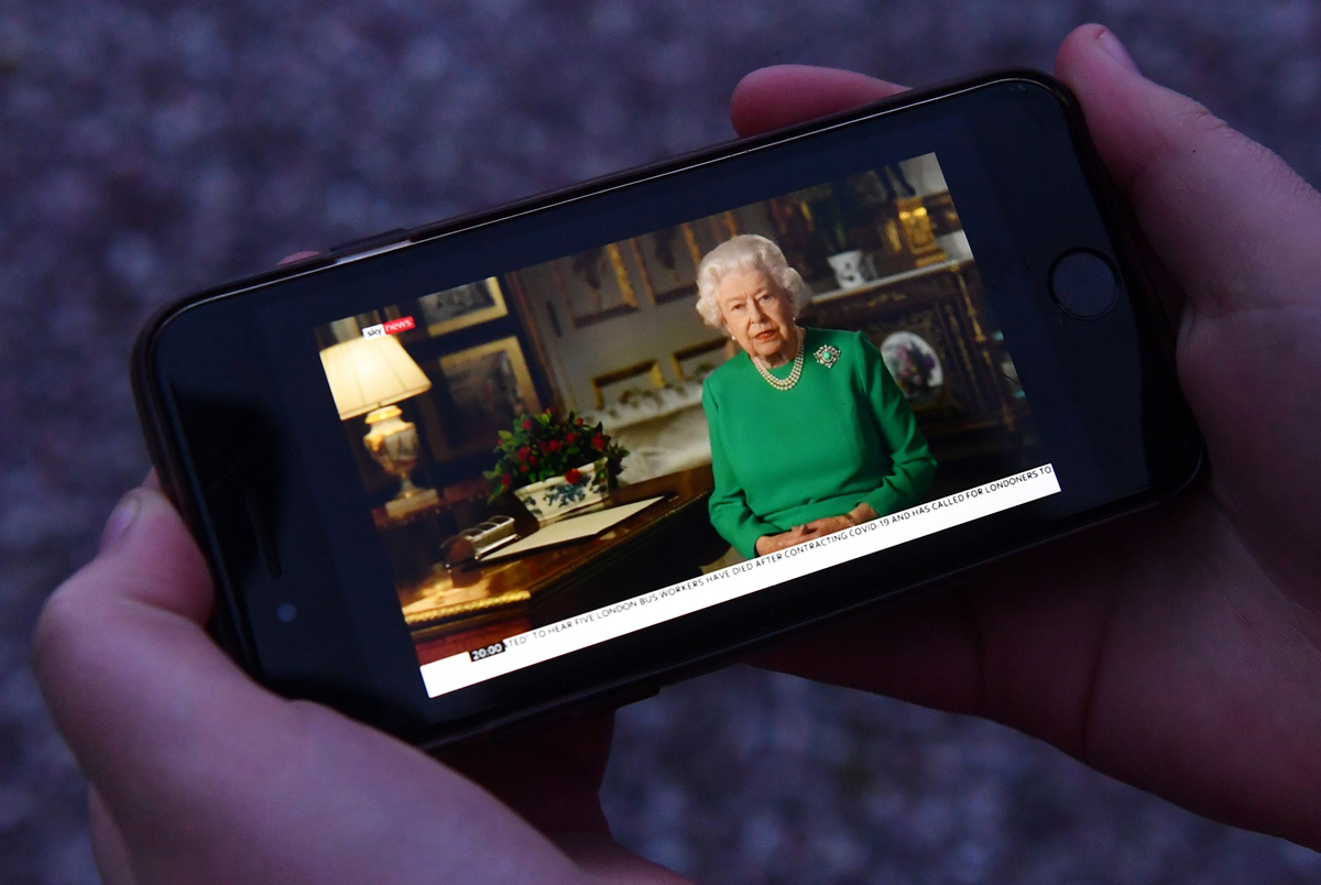 A viewer holds a mobile phone playing Queen Elizabeth II's special address to the nation regarding the pandemic on April 5, 2020 (PAUL ELLIS/AFP via Getty Images)