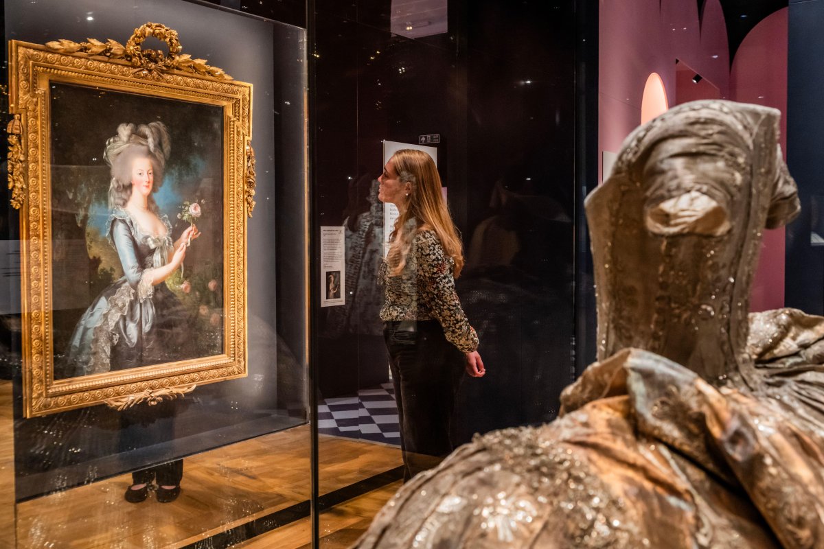 A visitor views a portrait of Marie Antoinette by Élisabeth Vigée Le Brun, with a wedding dress belonging to Queen Hedvig Elisabeth Charlotte of Sweden in the background, in the new Marie Antoinette Style exhibition at the Victoria & Albert Museum in London on September 16, 2025 (Guy Bell/Alamy)